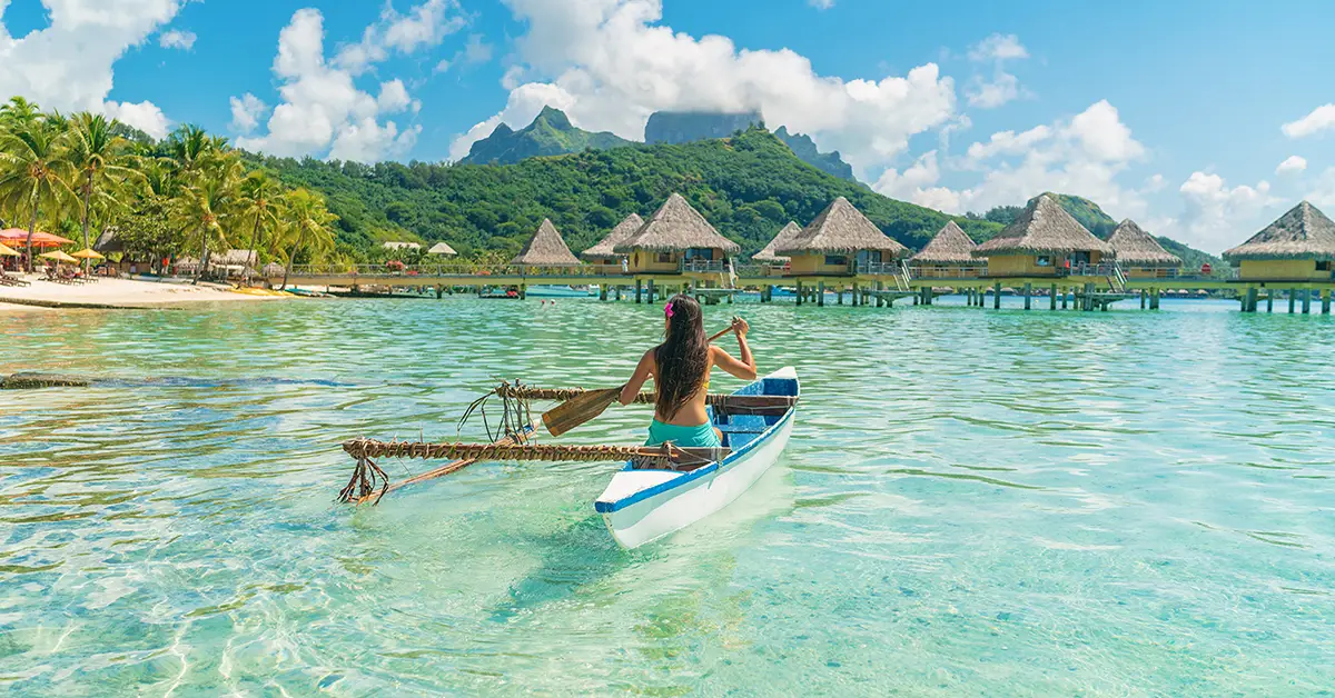 Kayaker drifting past overwater bungalows in a turquoise lagoon